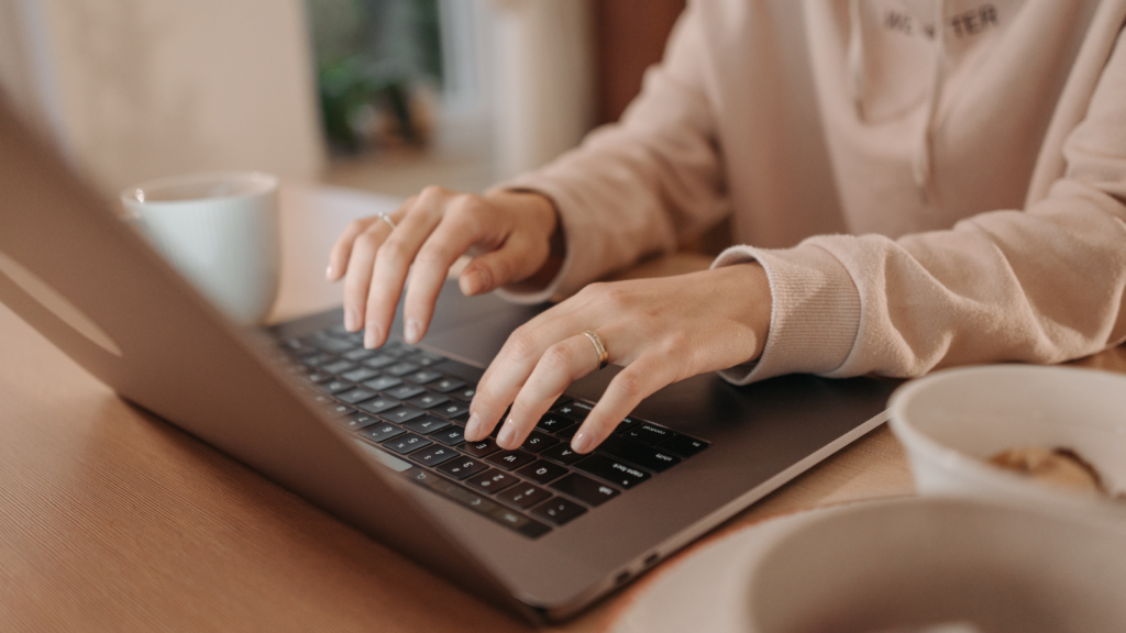 Stock photo from pexels by Pavel Danilyuk of a woman in a light beige hoodie typing on a laptop