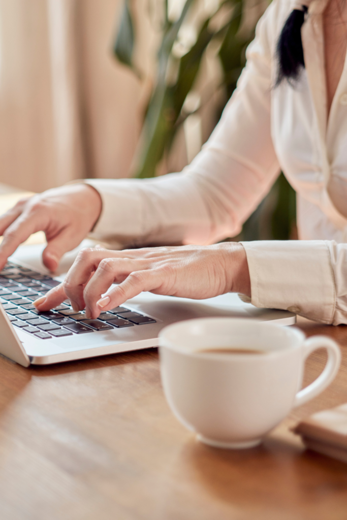 Stock photo from Canva by Hunur at Getty Images of a woman in a white shirt typing on a laptop