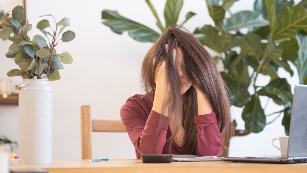Stock photo from Canva by yavdat at getty images of a woman at a table with her head in her hands