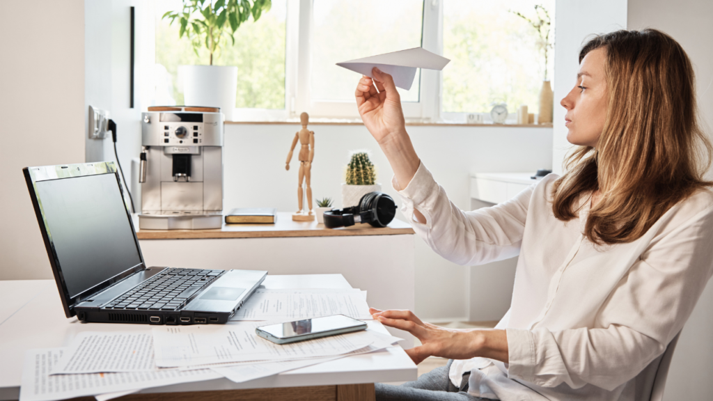 Stock photo from Canva by aliaksandrbarysenka of a woman sitting on a chair, playing with a paper plane procrastinating