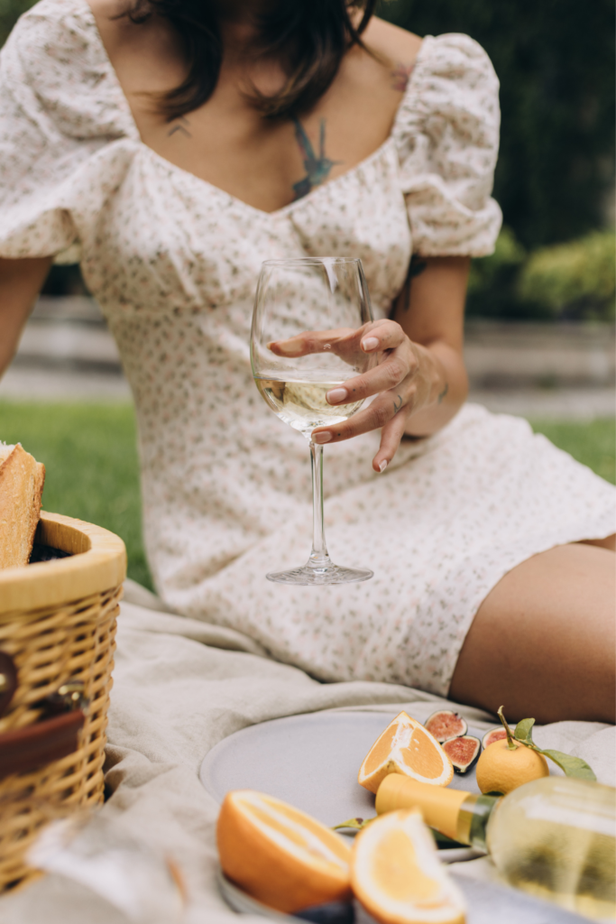 Stock photo from Canva by Carolin Voelker of a woman in a white dress sitting on a beige picnic blanket holding a glass of juice