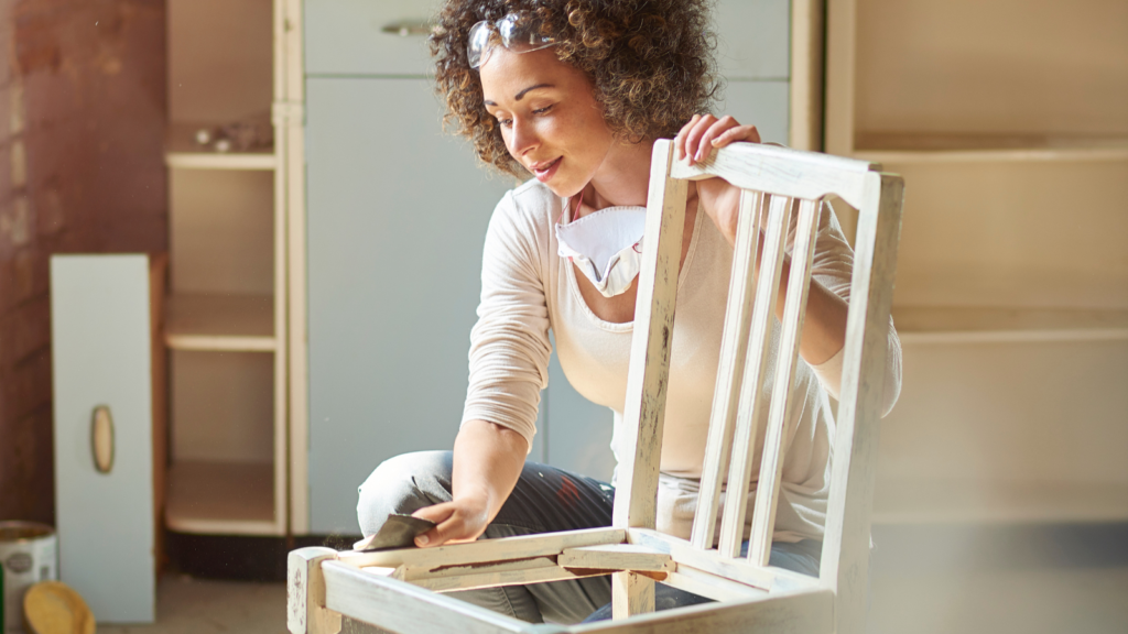 Stock photo from Canva by sturti at Getty Images of a woman sanding down a white chair frame