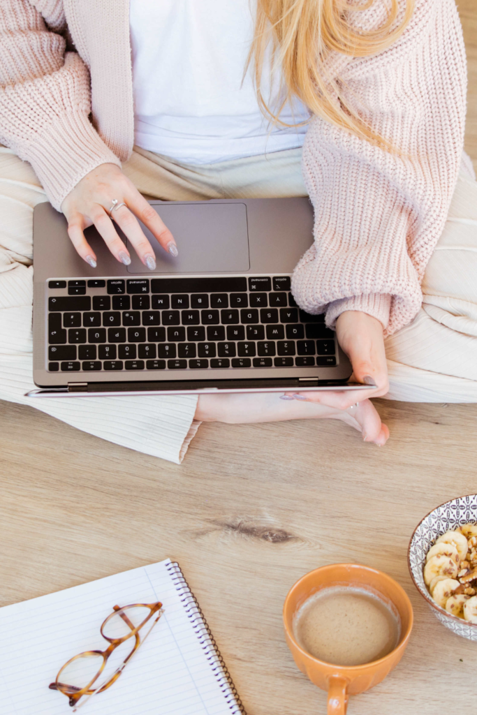 Stock photo from Canva by Emma Rahmani of a woman working on a a laptop while sitting on the floor wearing comfy lounge clothes that are pink and white