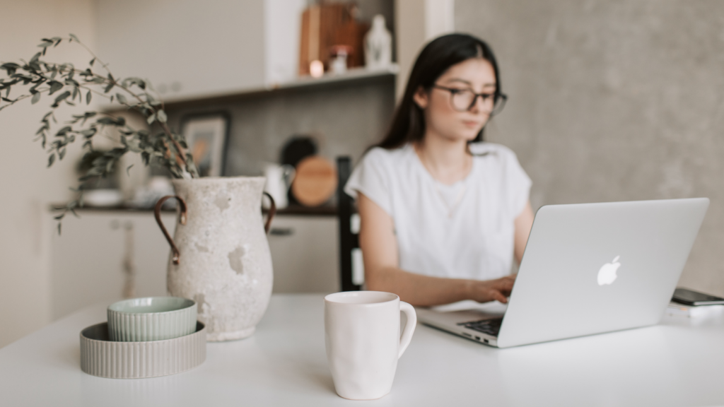 Stock photo from Canva by Vlada Karpovich of a woman sitting at a dining room table working on a silver apple macbook.