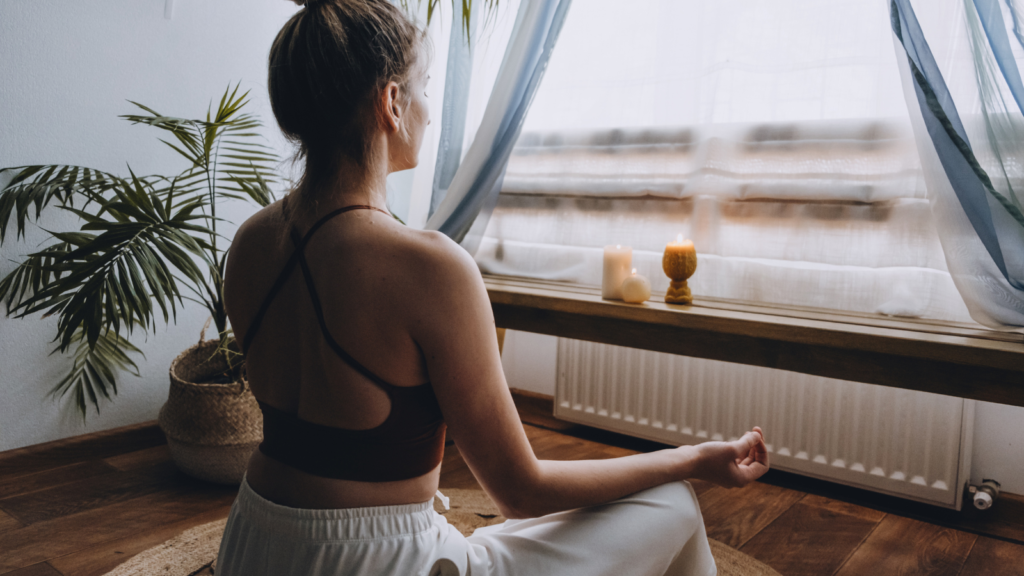 Stock photo from Canva by irynakhabliuk of a woman wearing workout clothes with her blond hair in a bun, sitting on the floor meditating