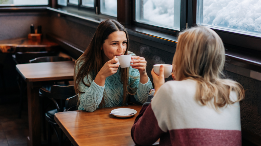 A stock photo from Canva of two woman having coffee at a round coffee shop table