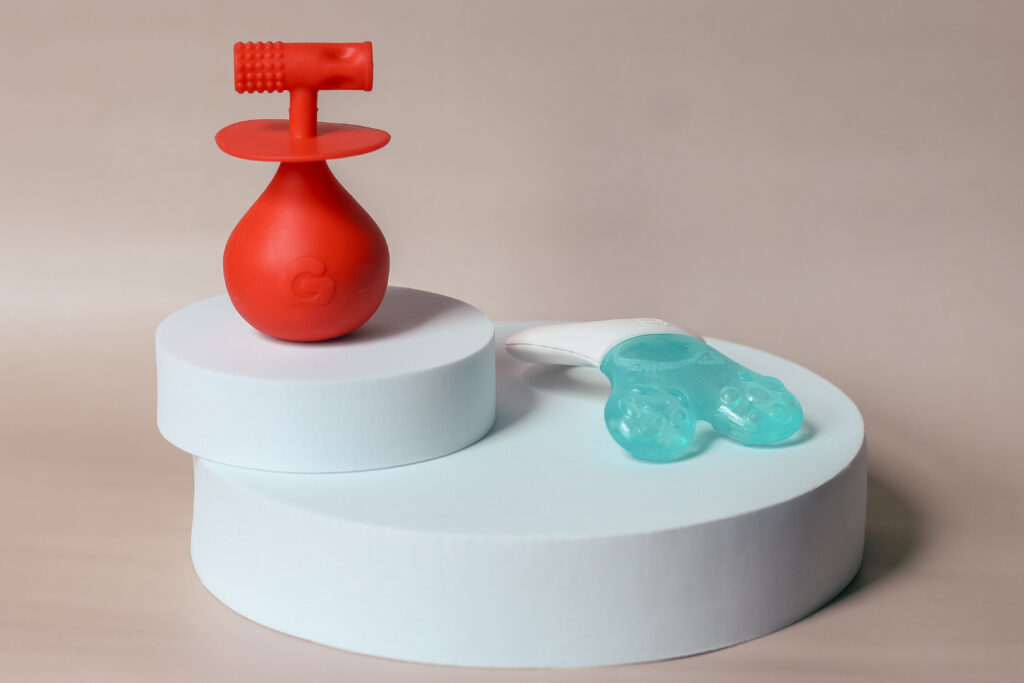 Photo of the Gummee Molar Mallet teething toy and MAM Mini Cooler teether on a round white pedestal taken by Ofaglasgowgirl