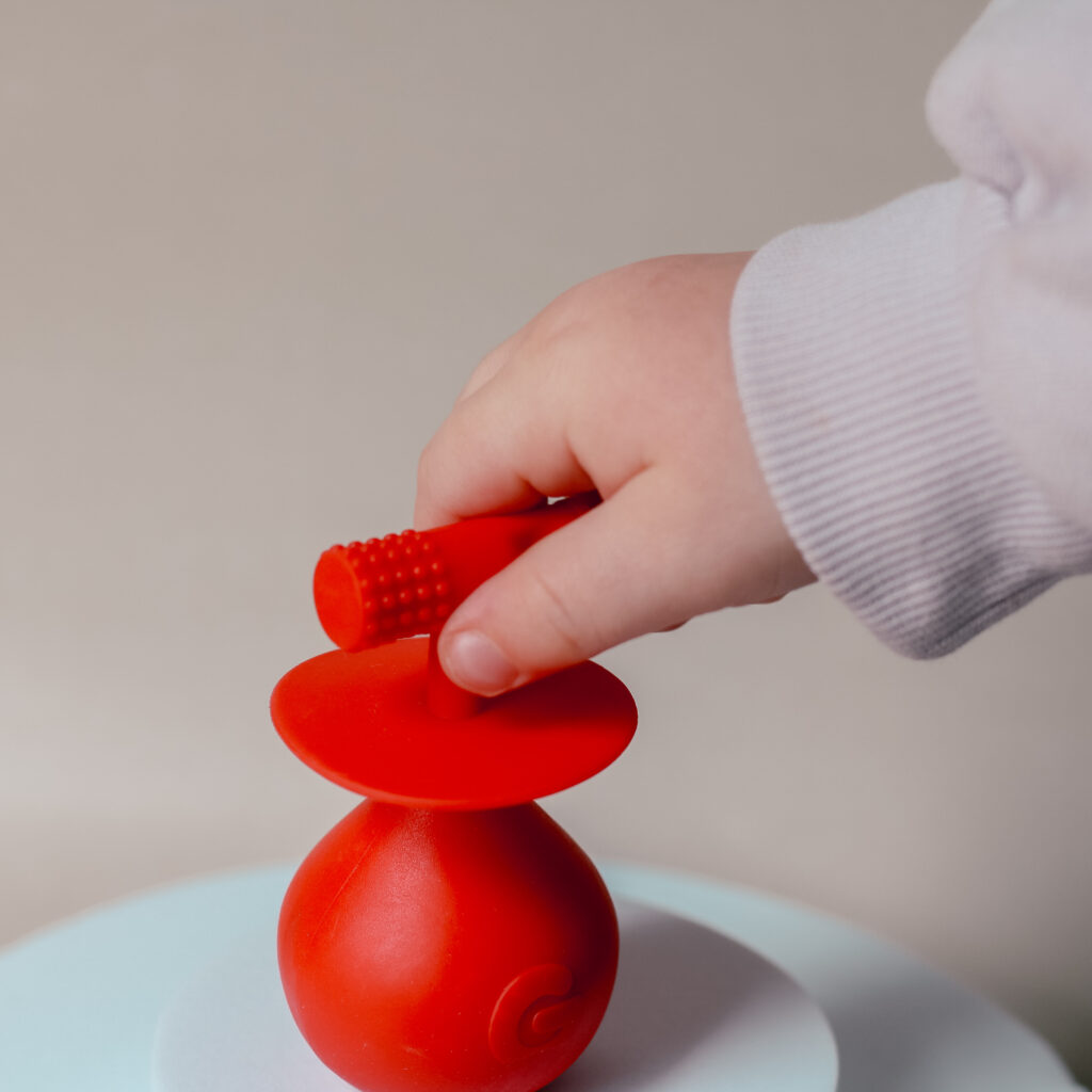 Close up photo of the red Molar Mallet Teething Toy from Gummee being grabbed by a babies hand, taken by Ofaglasgowgirl